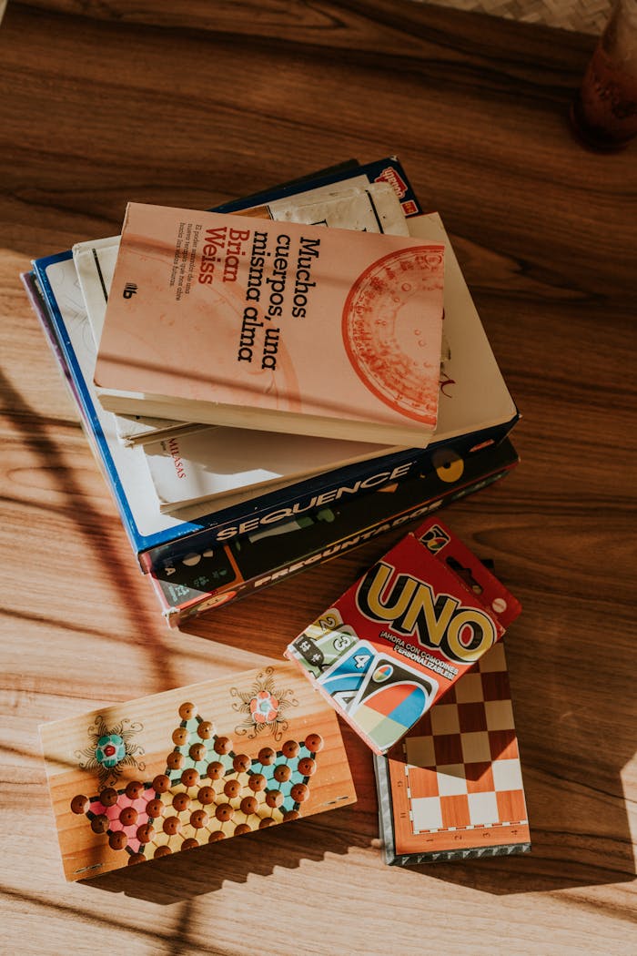 A cozy arrangement of books and board games on a sunlit wooden floor.