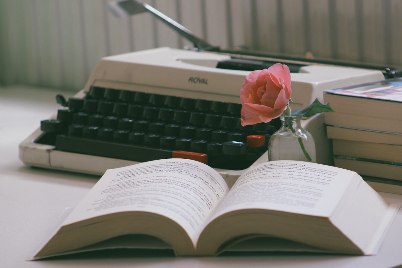Cozy vintage setting with a typewriter, open book, and pink rose in a vase.